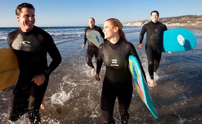 A group of surfers walking across the shoreline of the Pacific Ocean